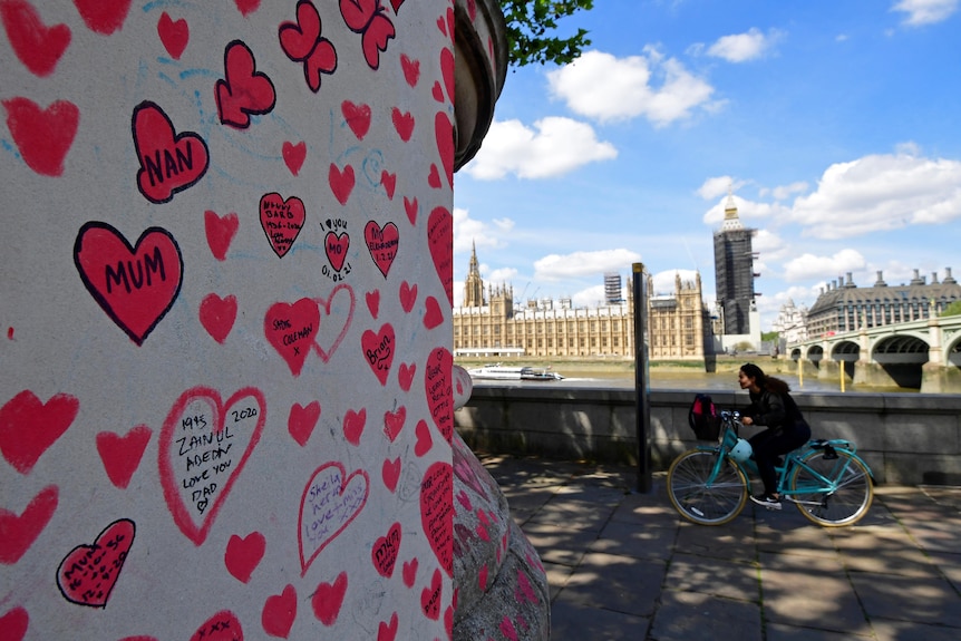 A cyclist rides past a memorial wall for COVID-19 victims in London.