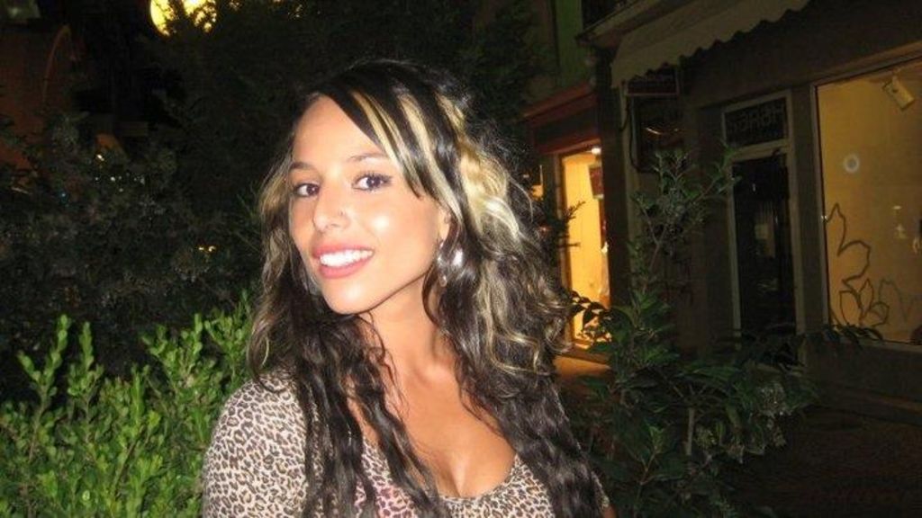 Woman with dark long wavy hair with golden streaks smiles big wearing hoop earrings and cheetah print top