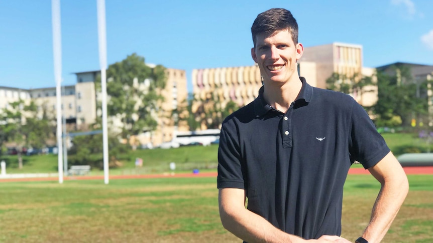 Justin Clarke standing on an AFL oval at the University of Queensland