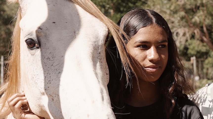 A girl with brown hair standing next to a white horse.