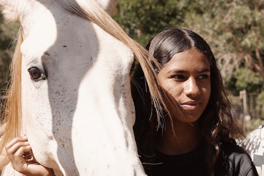 A girl with brown hair standing next to a white horse 