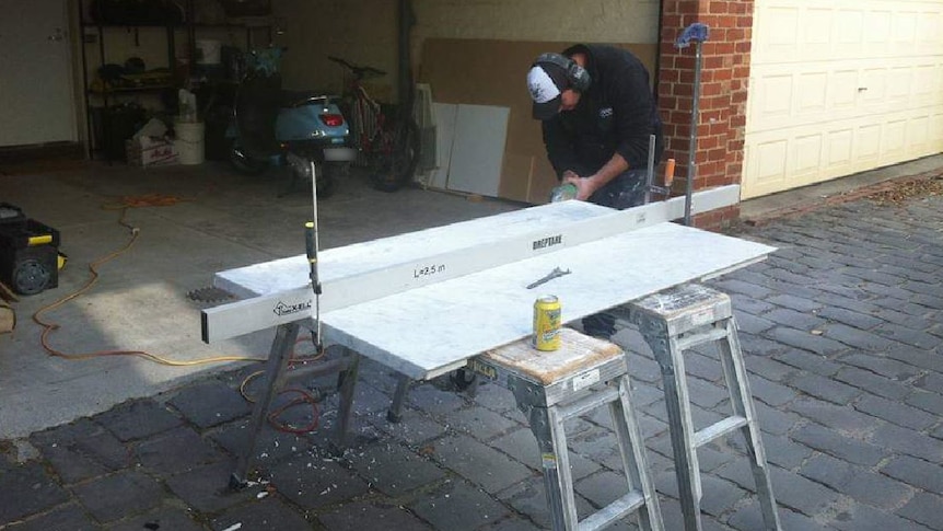 A man works on a stone kitchen benchtop outside.