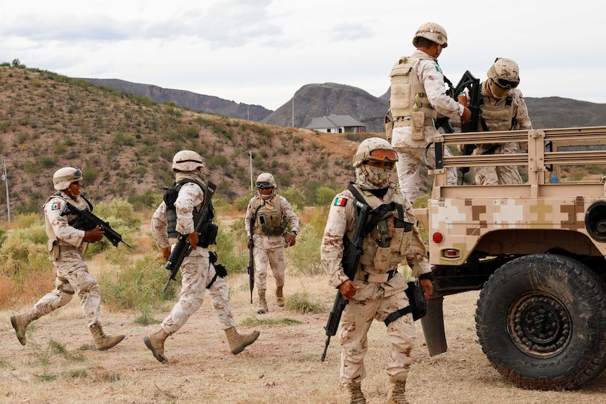 Six soldiers wearing camouflage uniforms are outside the Mormon community