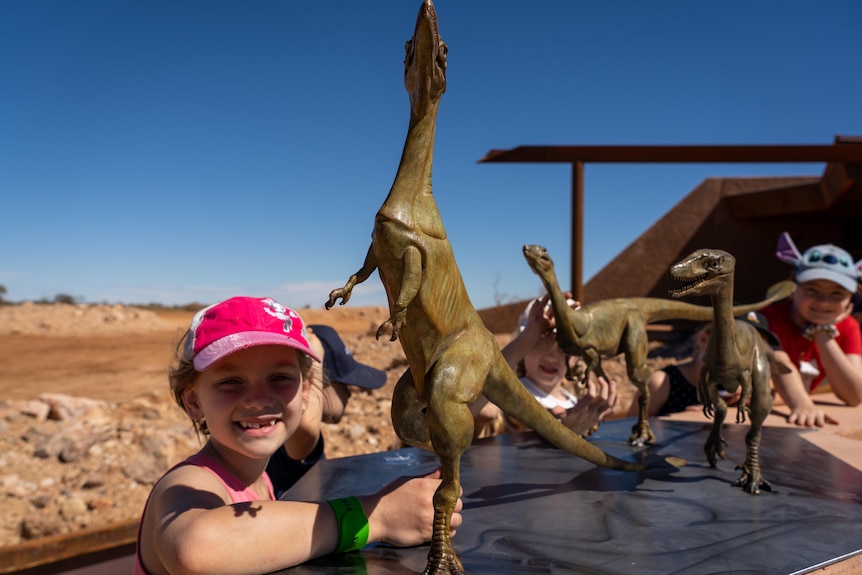 A group of kids pose for photos with tiny dinosaur statues.