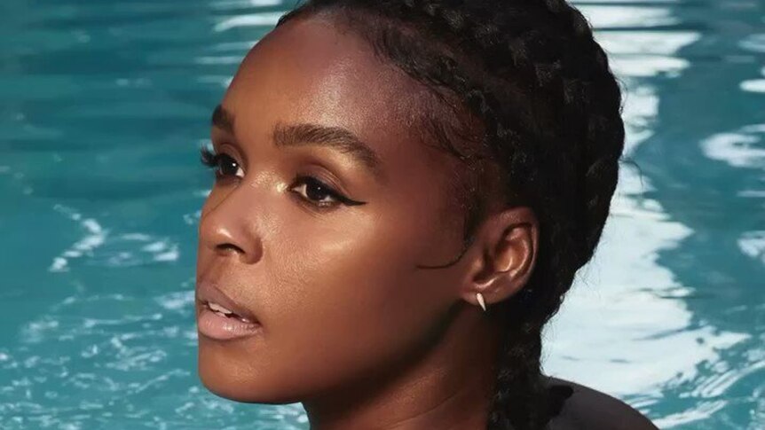 A closeup of a woman with brown skin. She is in a pool and looking over her shoulder towards the camera.