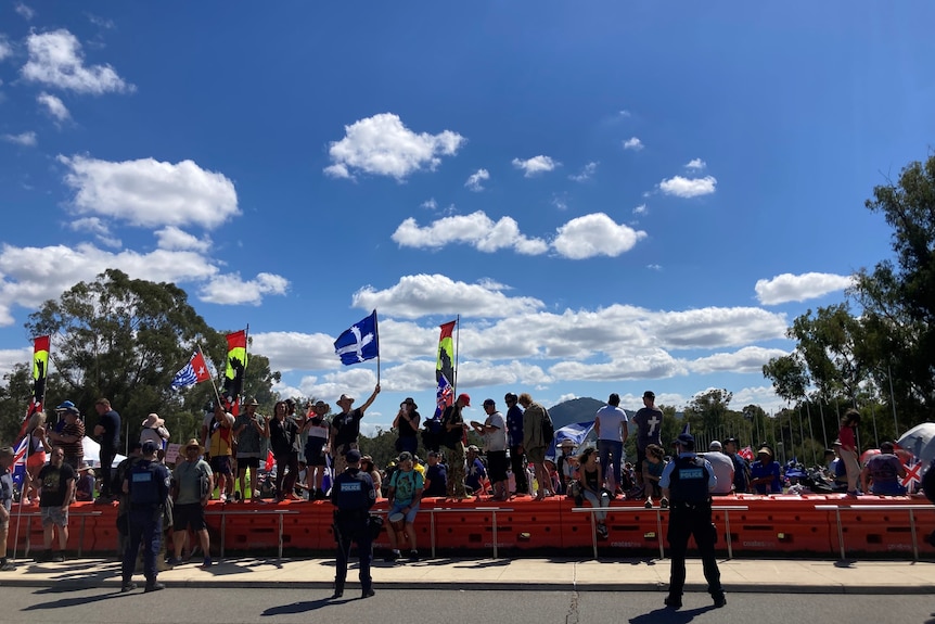 Protesters wave various flags behind concrete barricades.