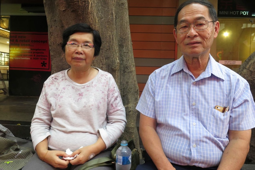 Mr Xiao and his wife sit on a bench in a mall.