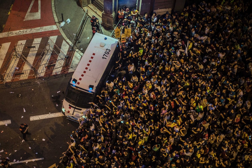An aerial photograph shows protestors pushing up against a police van in Barcelona.