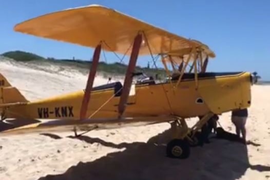 A yellow Tiger Moth plane parked on the sand at a beach.