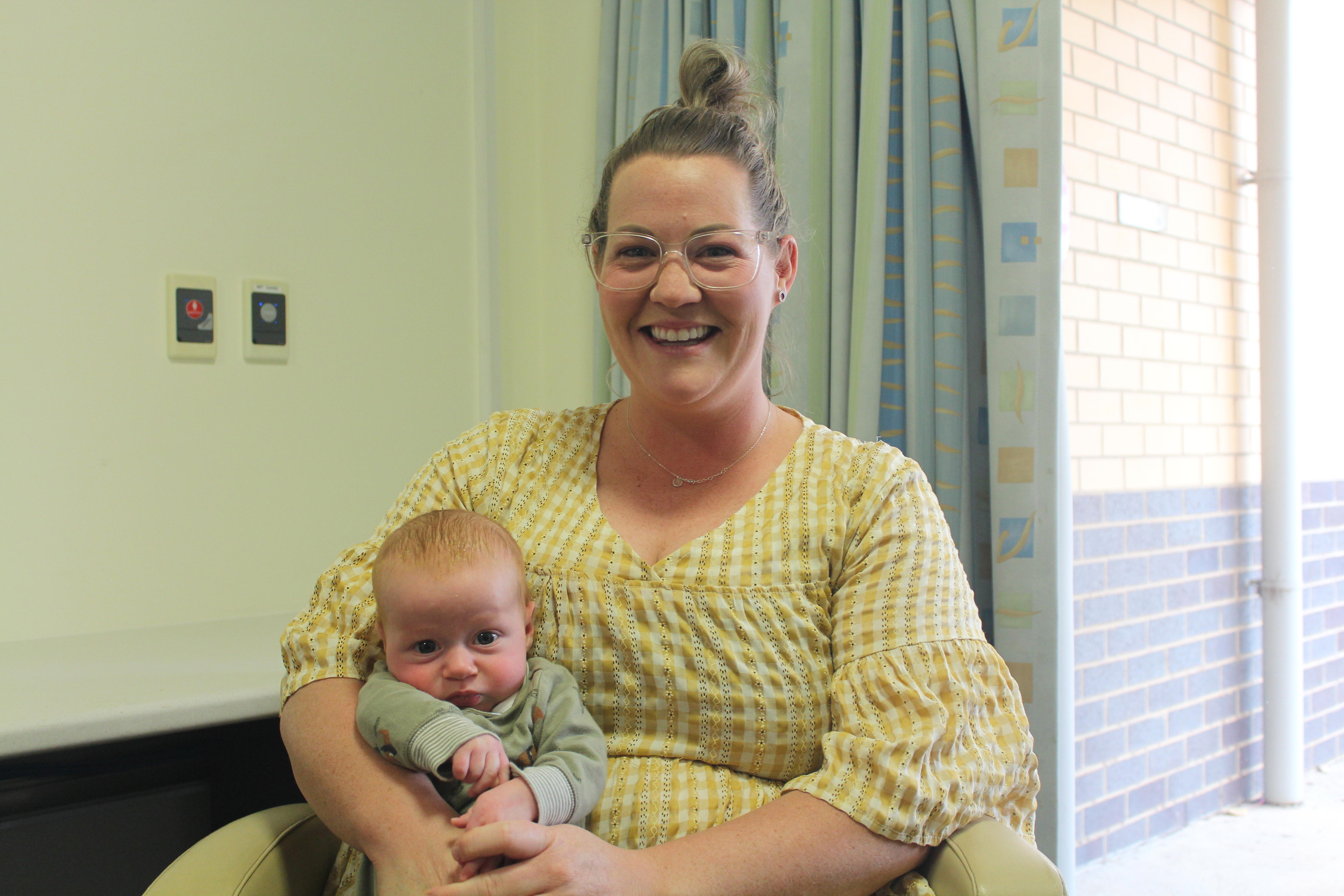 A mum holds a baby boy while sitting in a chair. 