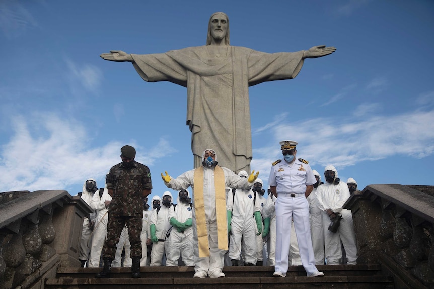 Catholic Priest Omar, center, leads a prayer as soldiers pause from disinfecting the Christ the Redeemer area,