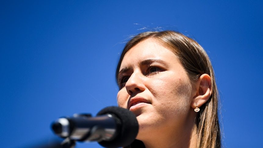 A woman with brown hair speaking into a microphone with blue sky in the background