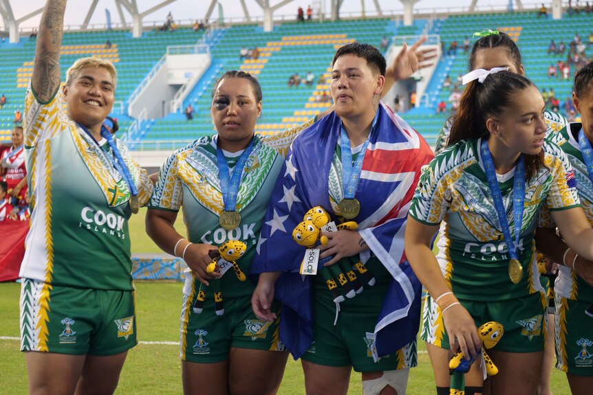A group of Cook Islands women in green smile and hold their medals.