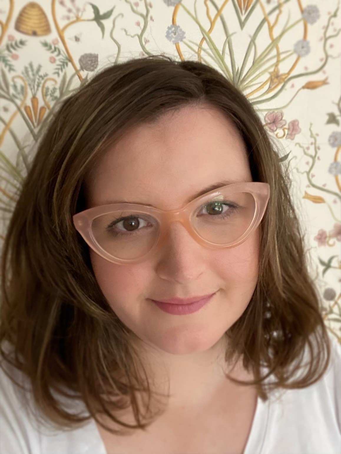 Close-up headshot of Gemma, with shoulder-length brown hair and pink 1960s style glasses, smiling slightly.
