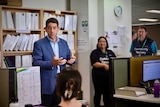 Queensland treasurer Cameron Dick stands in a Community Recovery office and speaks with staff.