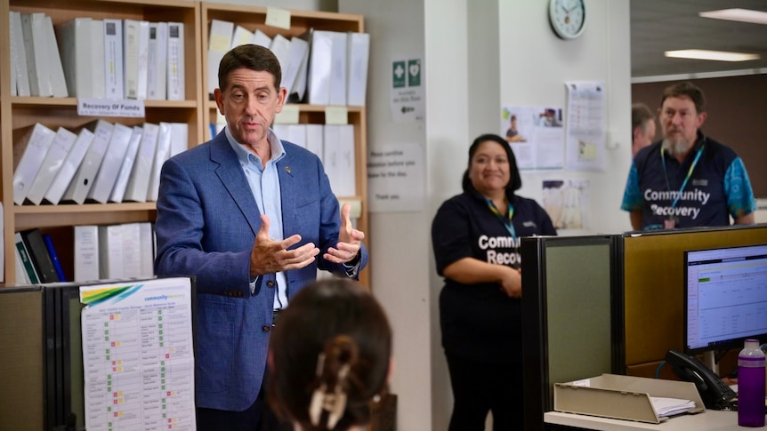 Queensland treasurer Cameron Dick stands in a Community Recovery office and speaks with staff.