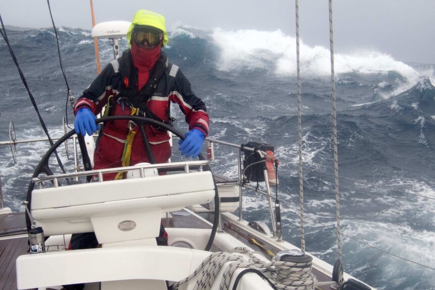 Sailor at helm of yacht in large swell.
