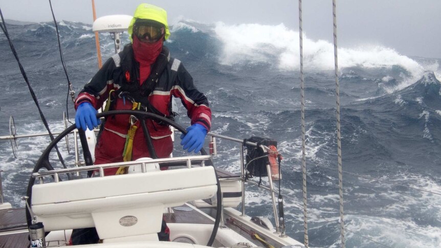 Sailor at helm of yacht in large swell.