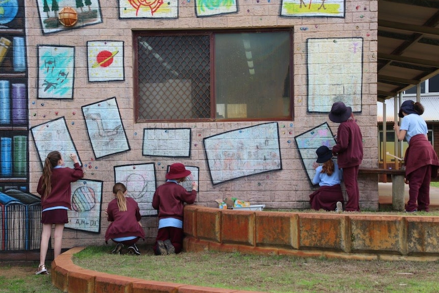 Children use chalk to draw on a wall at West Greenwood Primary School.