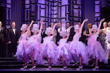 Dancers in pink tutus on stage in a row under purple lights