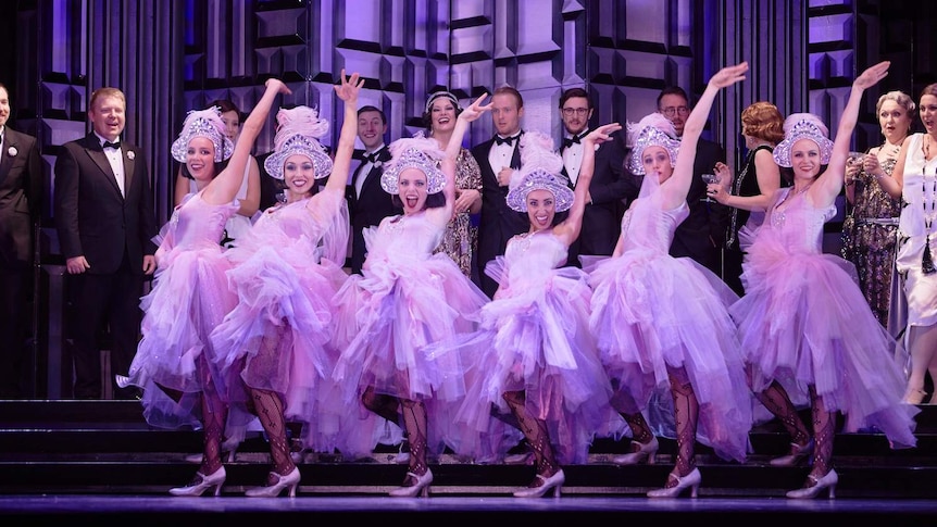 Dancers in pink tutus on stage in a row under purple lights