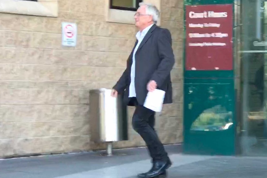 A man wearing a suit jacket, and untucked, open-neck shirt, walks out of court