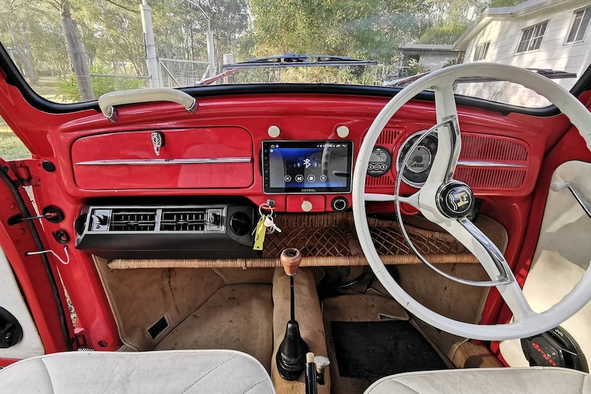 A car interior with red dash, white upholstery, and a large LCD screen