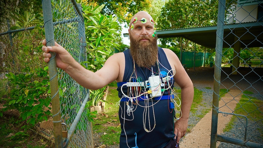 Man with medical cords stuck to his face and chest with a tube through his nose