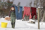 A man stands in deep snow as he hangs clothes on his washing line.