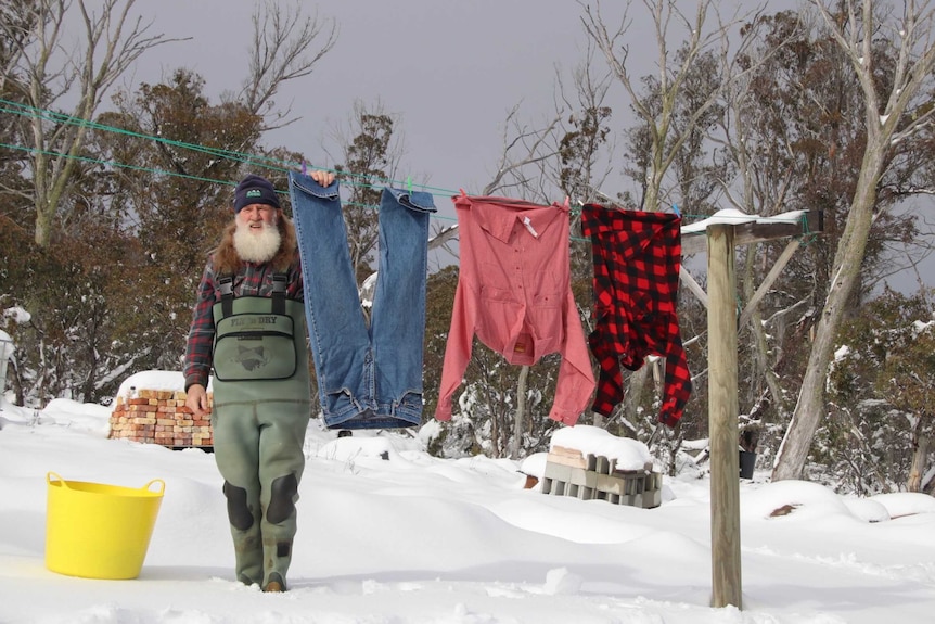 A man stands in deep snow as he hangs clothes on his washing line.