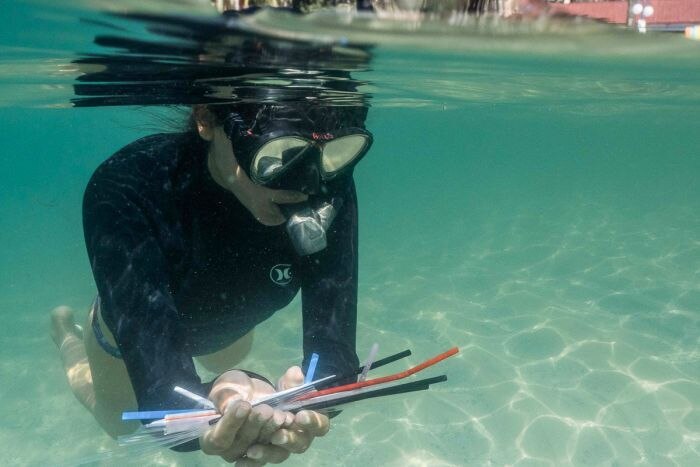 A diver is under water holding plastic straws they collected