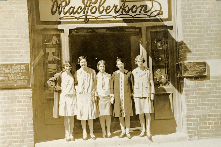 Four women stand outside a shop. Black and white photograph.