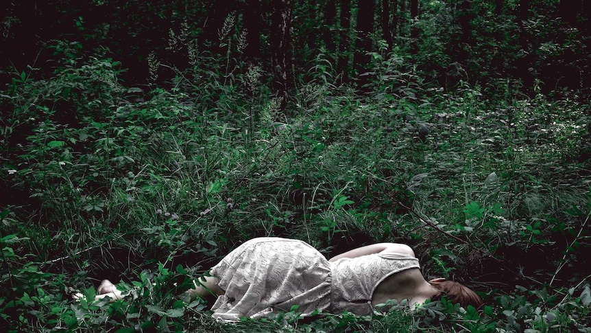 Young woman lies face away from the camera in a dark forest.