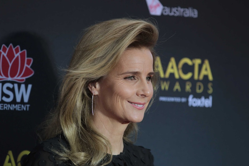 Headshot of woman with styled hair and makeup standing in front of event backdrop smiling for photographers