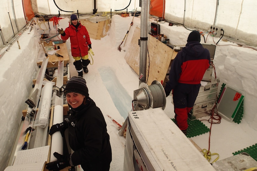Three people stand in an icy drench, turned into a makeshift lab looking at ice cores.