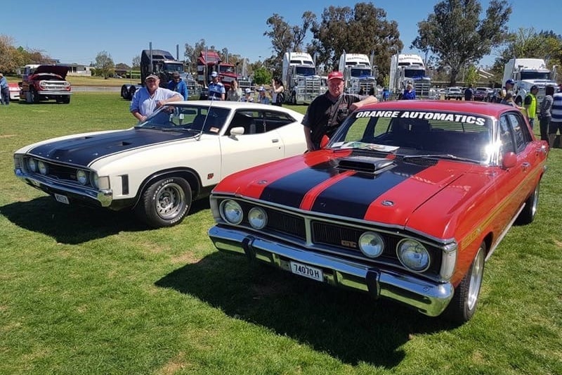 Two men each standing next to a Ford car at a car show.