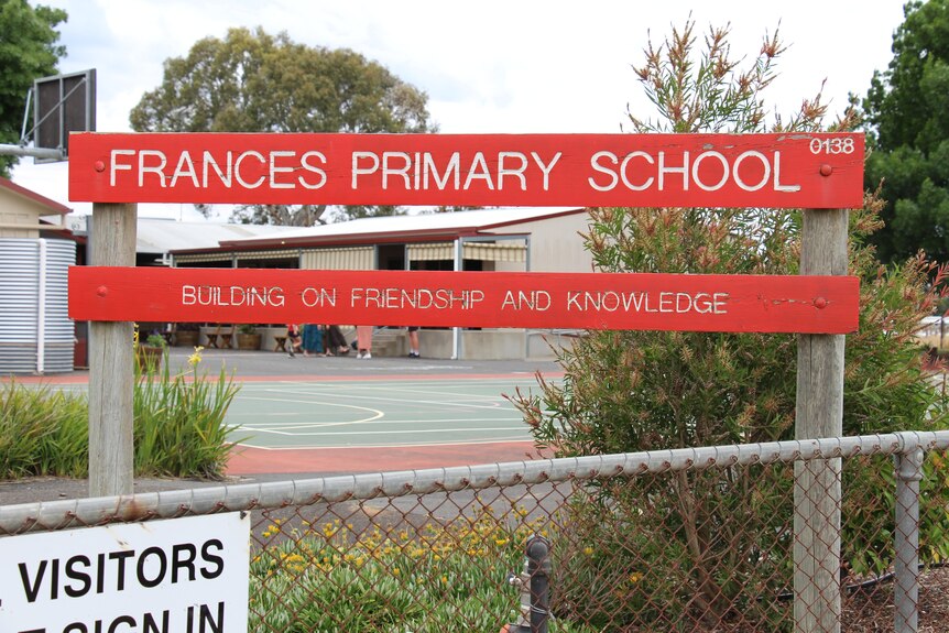 A red wooden sign reading "FranÃ§oise primary school" with buildings and basketball court in the background