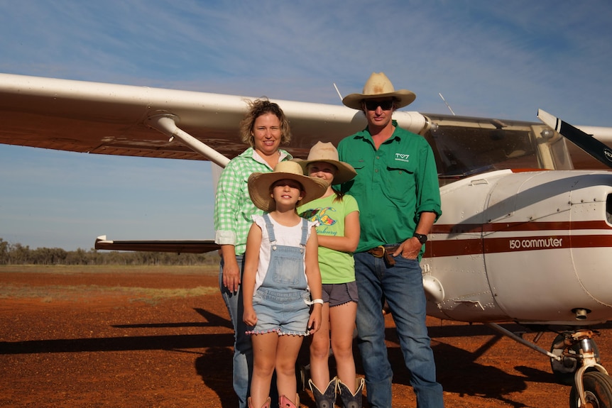 A family of four stand in front of a plane on an outback runway.