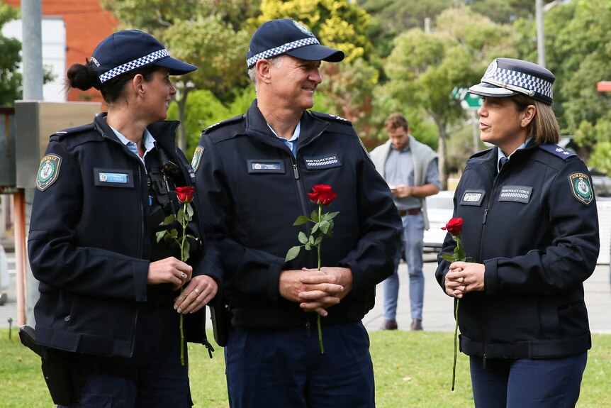 Police officers hold roses while speaking at an outdoor event.