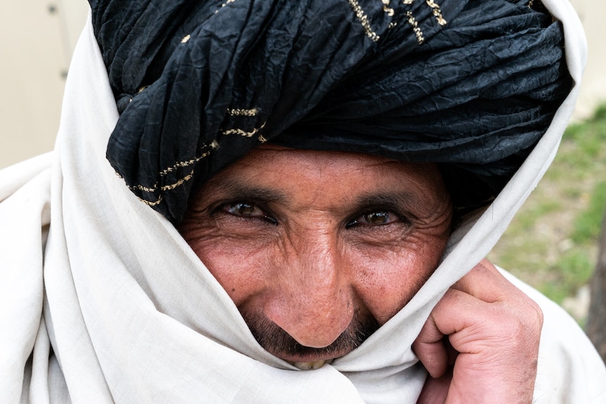 Close up of a smiling man with a black turban and a white cloth wound around his head