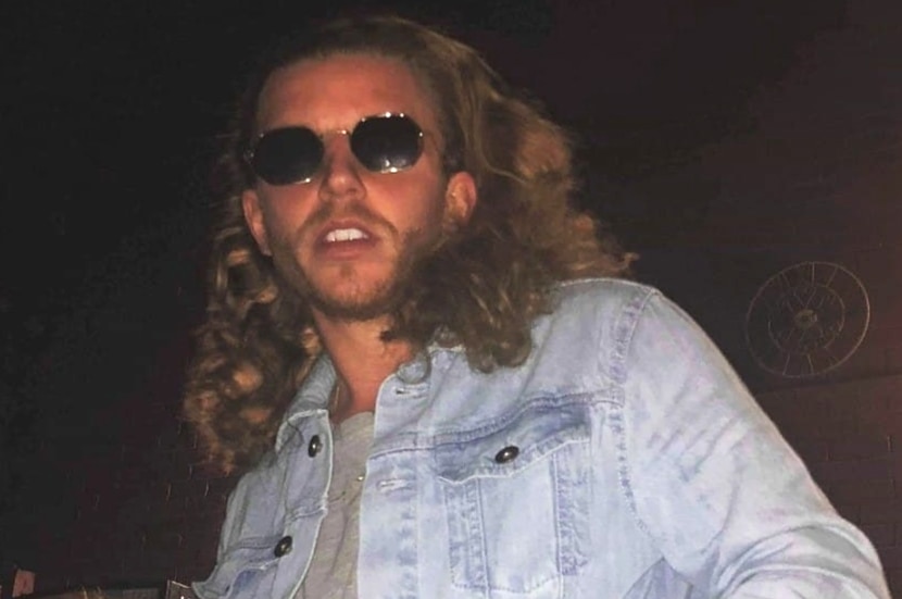 A young man in dark glasses and a denim jacket at a bar