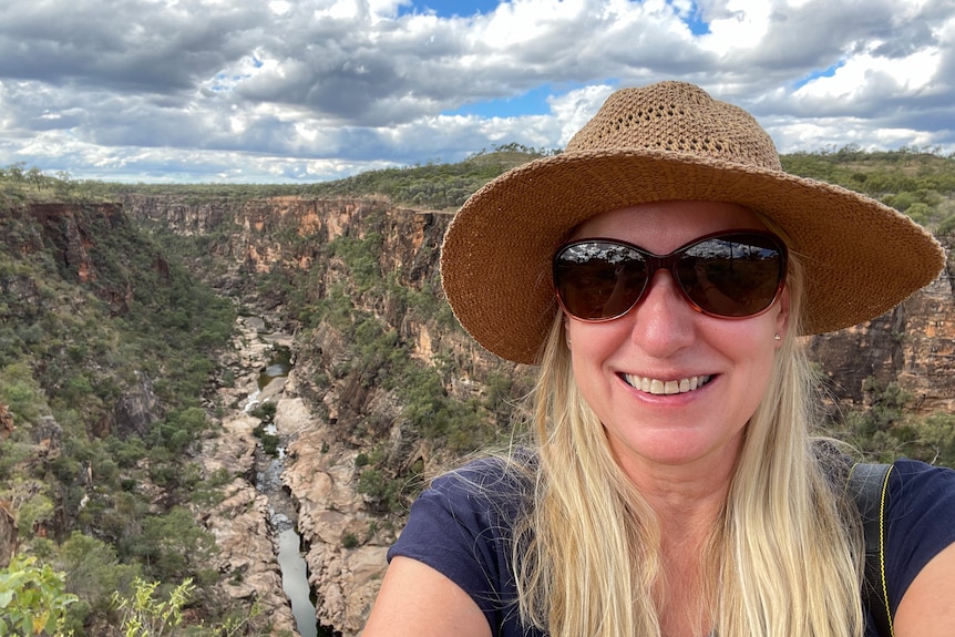 Selfie of woman in brim hat and sunglasses above a scenic gorge.