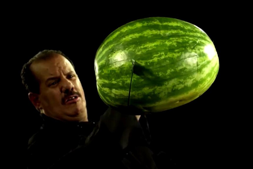 A man slicing through a watermelon mid-air. 