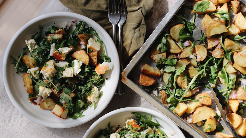 Two bowls of potato, haloumi and greens tray bake with the roasting pan used to make this vegetarian dinner.