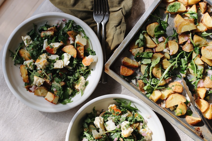 Two bowls of potato, haloumi and greens tray bake with the roasting pan used to make this vegetarian dinner.