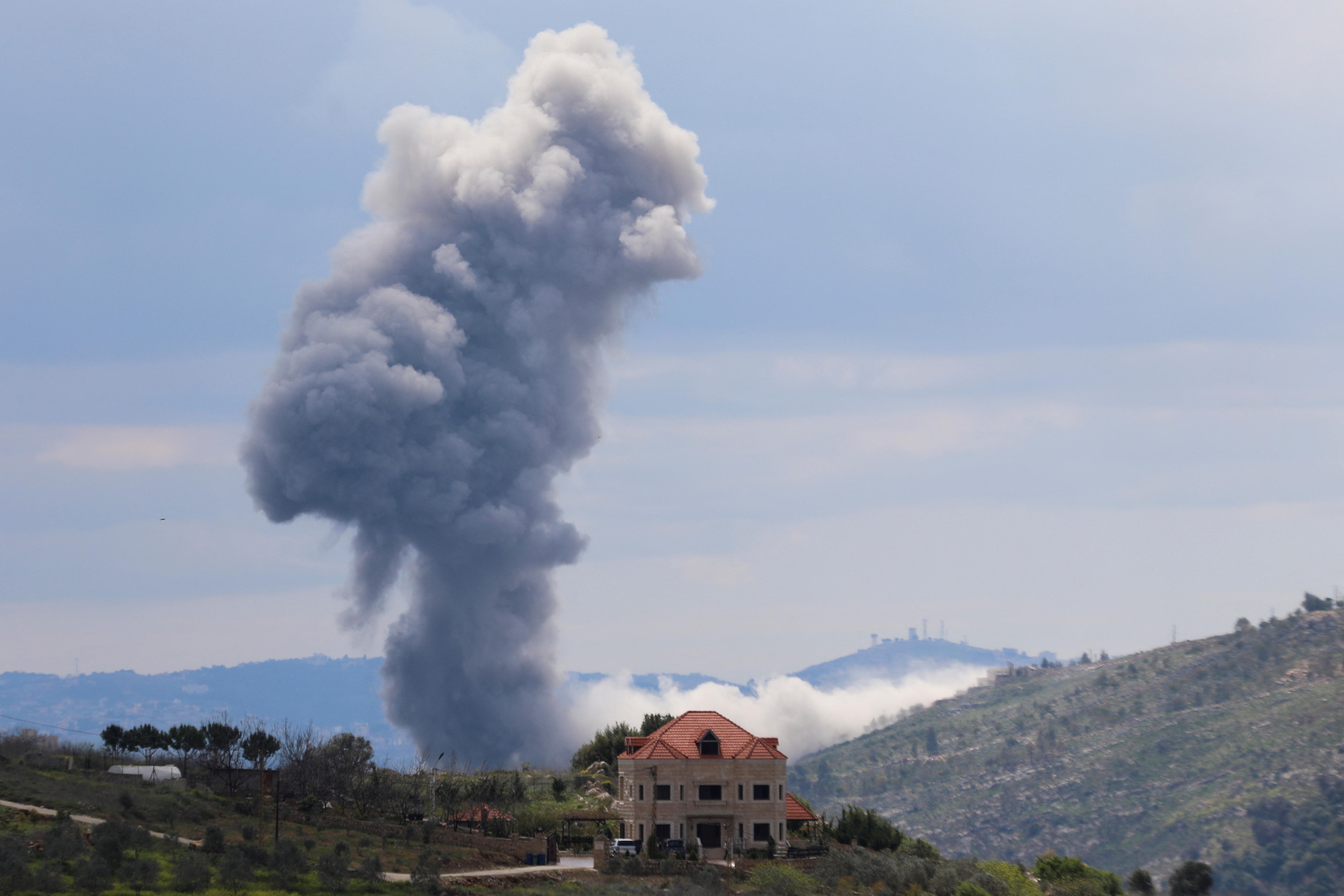Smoke rises close to a nearby house with surrounding hills