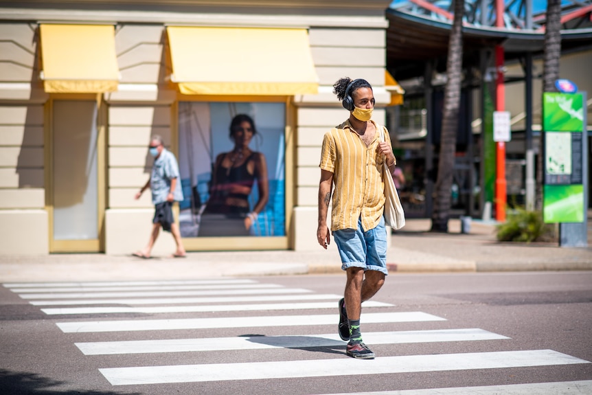 A man wearing a face mask walks across a crossing in the Darwin CBD.