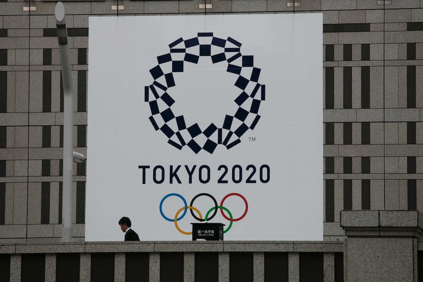 Un hombre pasa junto a una gran pancarta que promueve los Juegos Olímpicos de Tokio 2020.