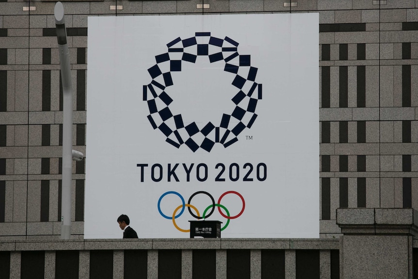 A man walks past a large banner promoting the Tokyo 2020 Olympics.