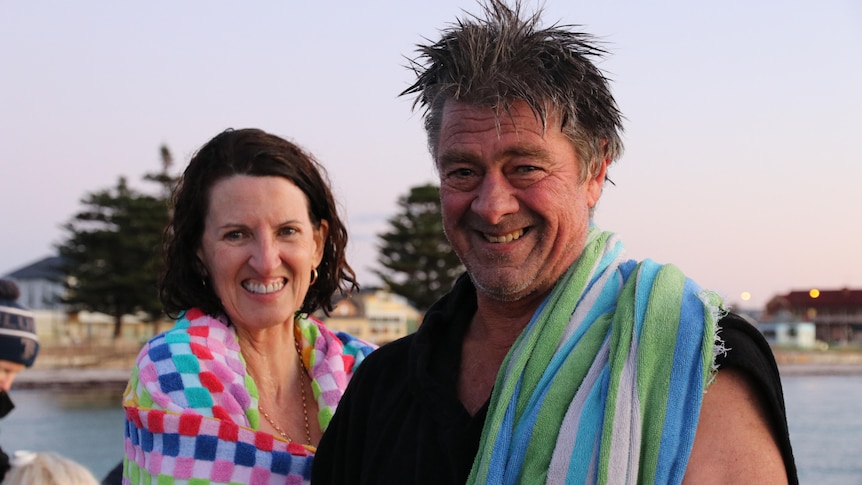 A woman and a man with towels around their neck stand at a jetty. 